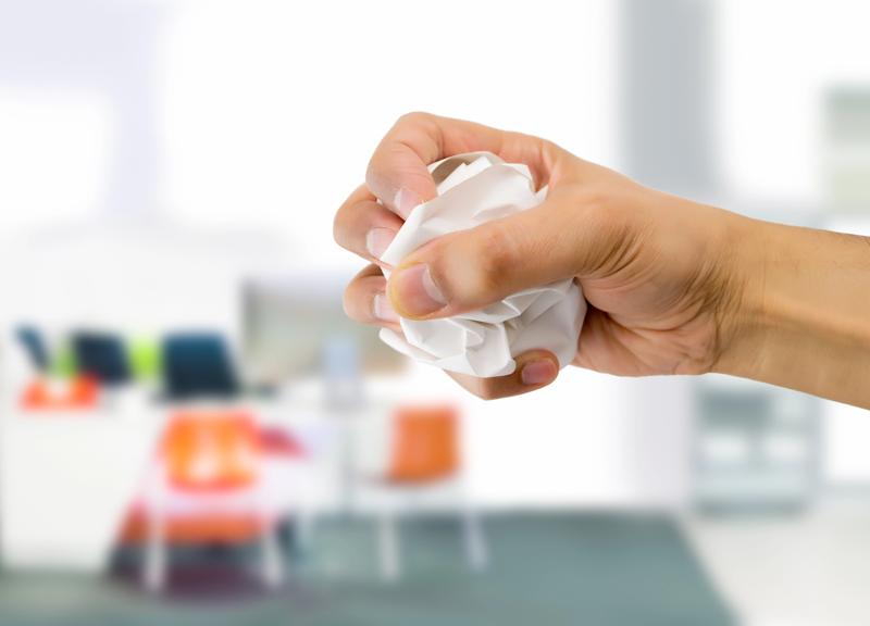 Main écrasant une feuille de papier symbolisant la destruction d’archives dans un environnement de bureau.