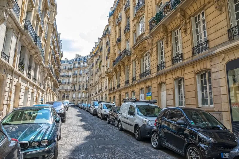 Rue typique de Paris avec des immeubles haussmanniens et des véhicules utilitaires stationnés, idéale pour illustrer une intervention de débarras.
