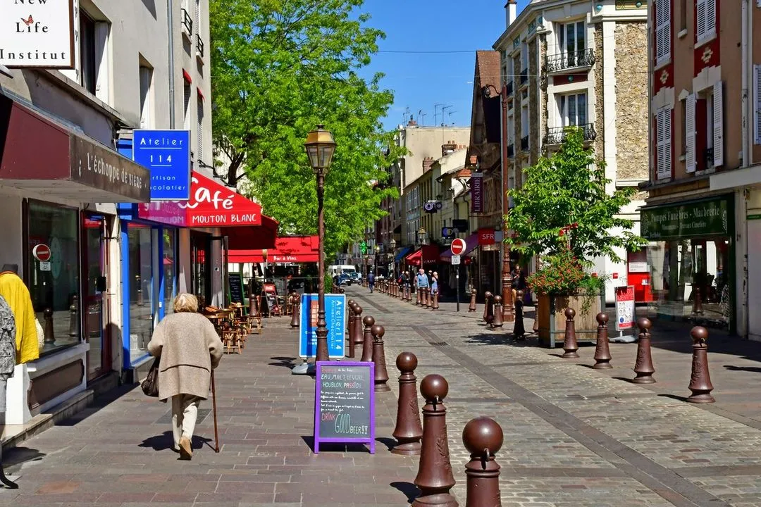 Rue commerçante animée à Poissy, dans les Yvelines, avec boutiques, terrasses de café et passants sur une voie piétonne pavée.