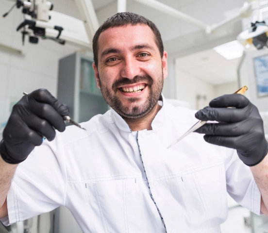 Smiling male doctor wearing black gloves and a white coat holding medical tools in a clinic.