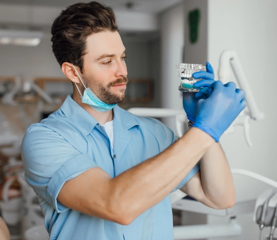 Male medical professional wearing blue gloves and scrubs examining a medical model in a clinic.