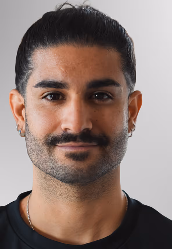 Portrait d'un homme avec une barbe et une moustache, cheveux attachés, portant des boucles d'oreilles et un t-shirt noir.