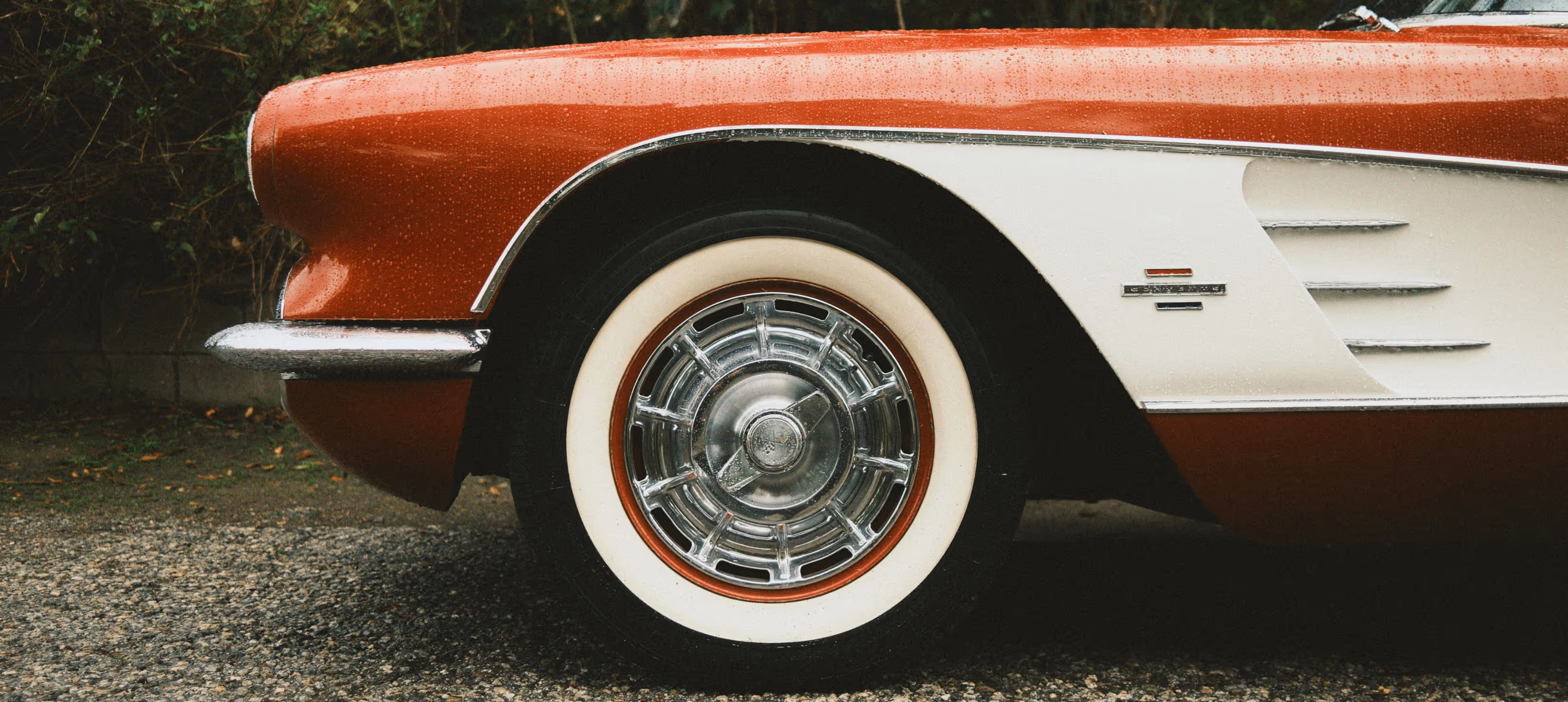 Gros plan sur la roue à bande blanche d'une voiture classique rouge et blanche mouillée par la pluie.