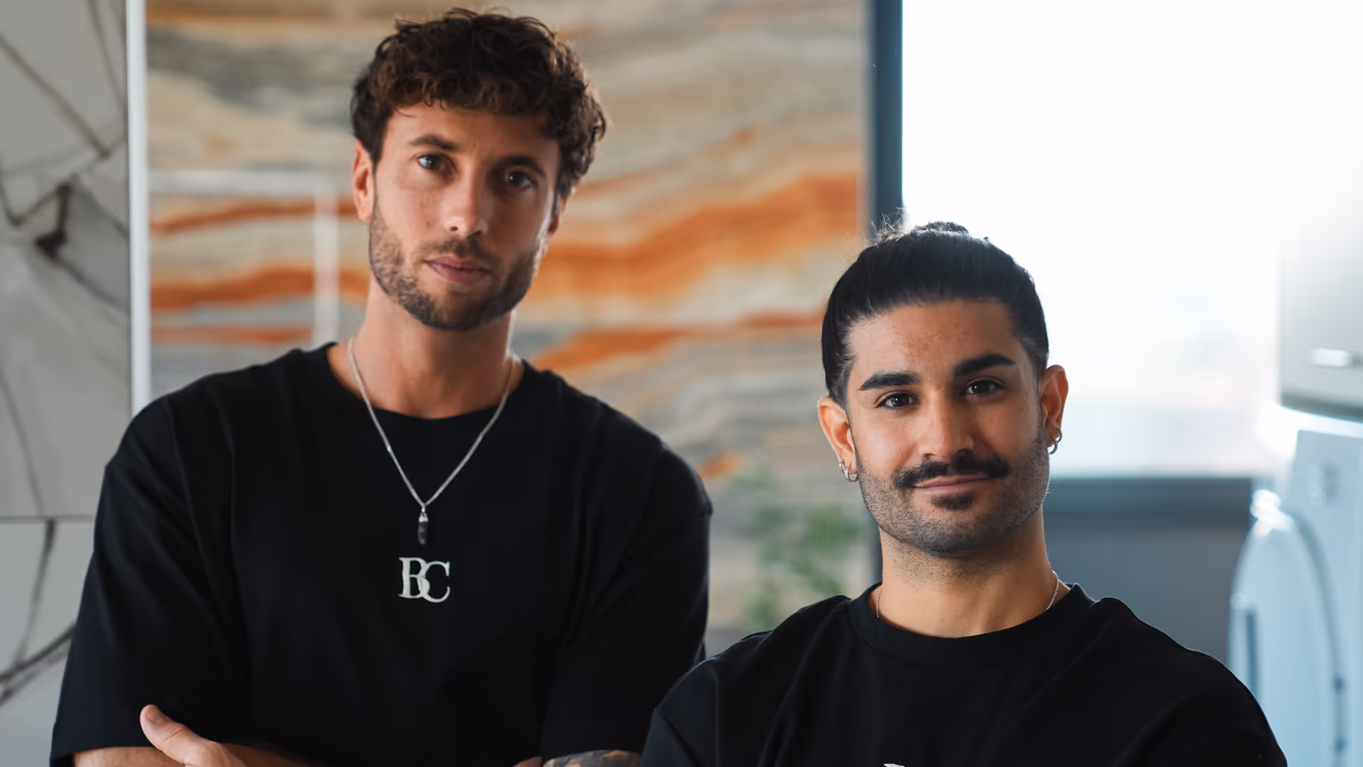 Les fondateurs portant des t-shirts noirs posant dans une pièce moderne avec un mur en marbre et une fenêtre en arrière-plan.