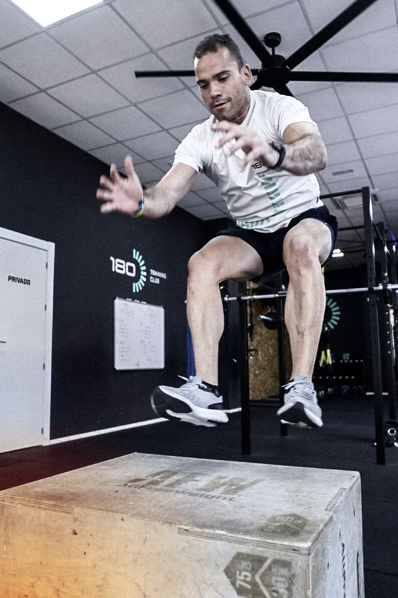 Hombre saltando sobre una caja de madera durante el entrenamiento funcional dentro en el centro de 180 Training Club.