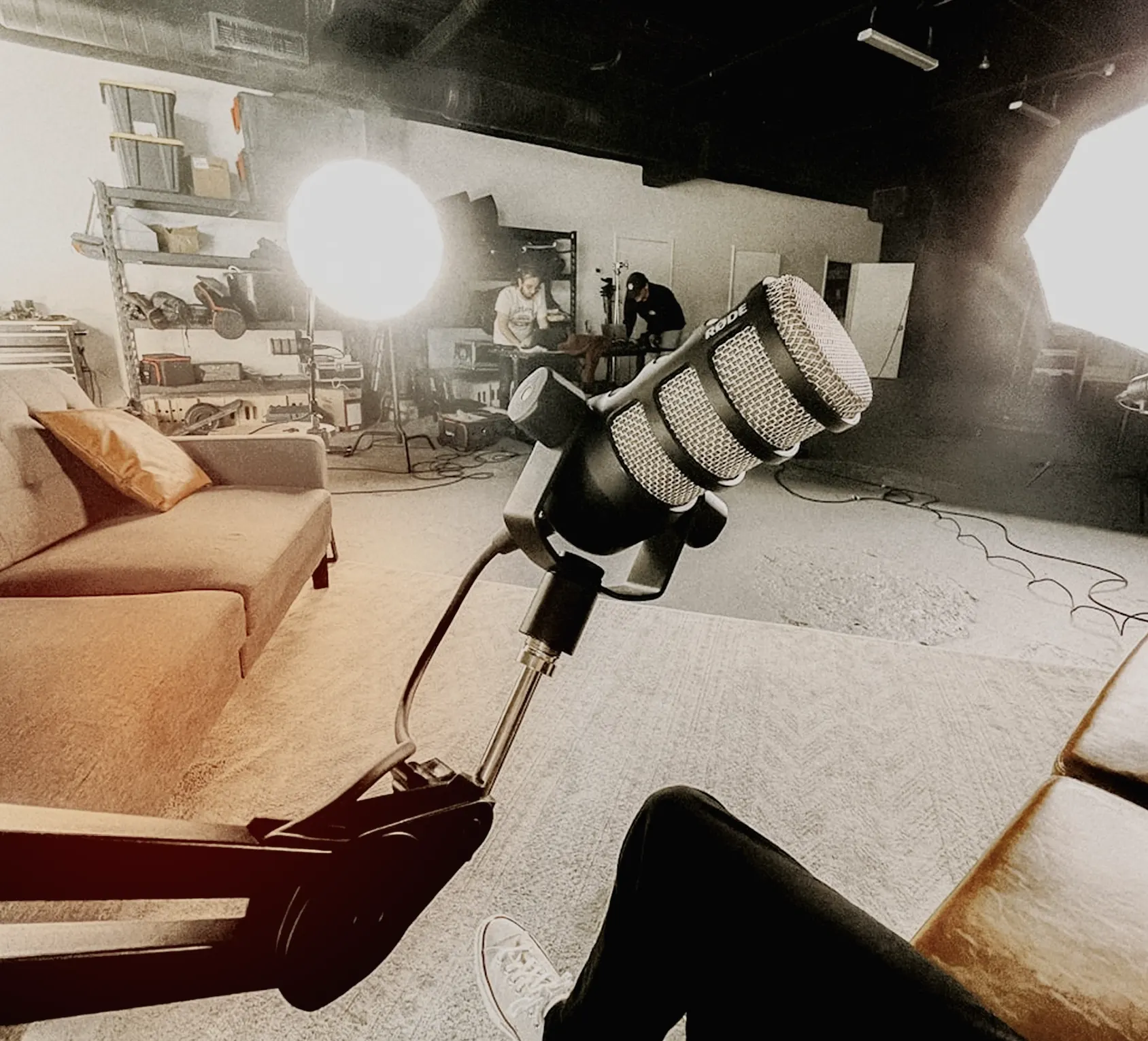 Micrófono Rode en un estudio con sofá, luces de iluminación y dos personas trabajando en el fondo donde se graba 180 podcast.