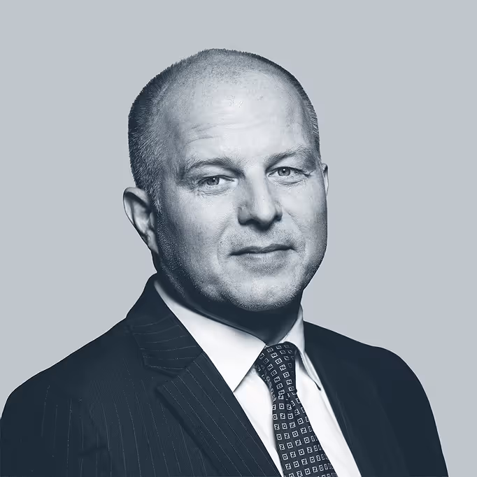 Portrait of a middle-aged man in a dark suit, white shirt, and patterned tie against a plain gray background.