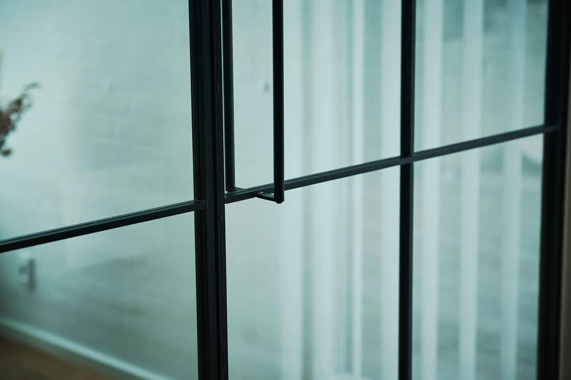 Nærbillede af en åben sort metal- og glasdør med sløret baggrund af en væg og vindue.