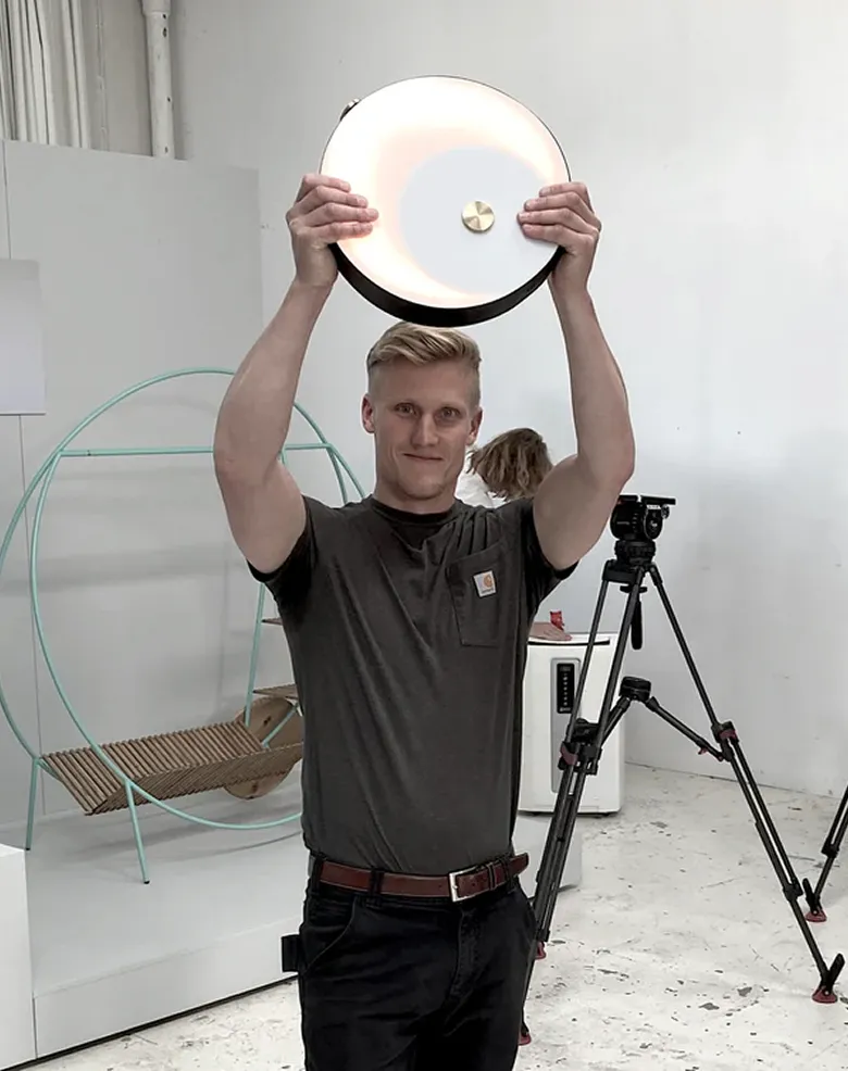 Mand holder en rund, oplyst lampe over sit hoved i et lyst rum med kameraudstyr i baggrunden.