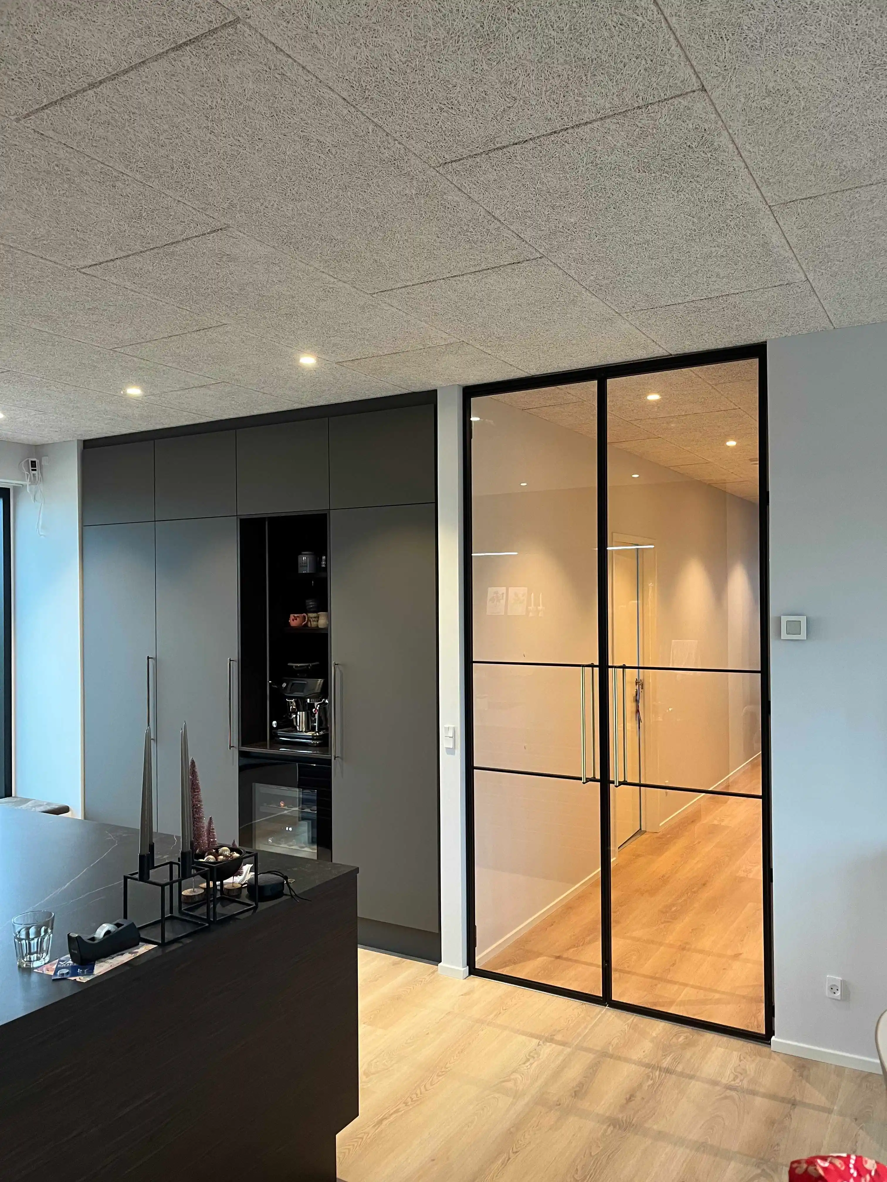 Moderne køkken med mørke skabe, en ø med dekorative lysestager og dobbelt glasdør med sort ramme til lys gang.