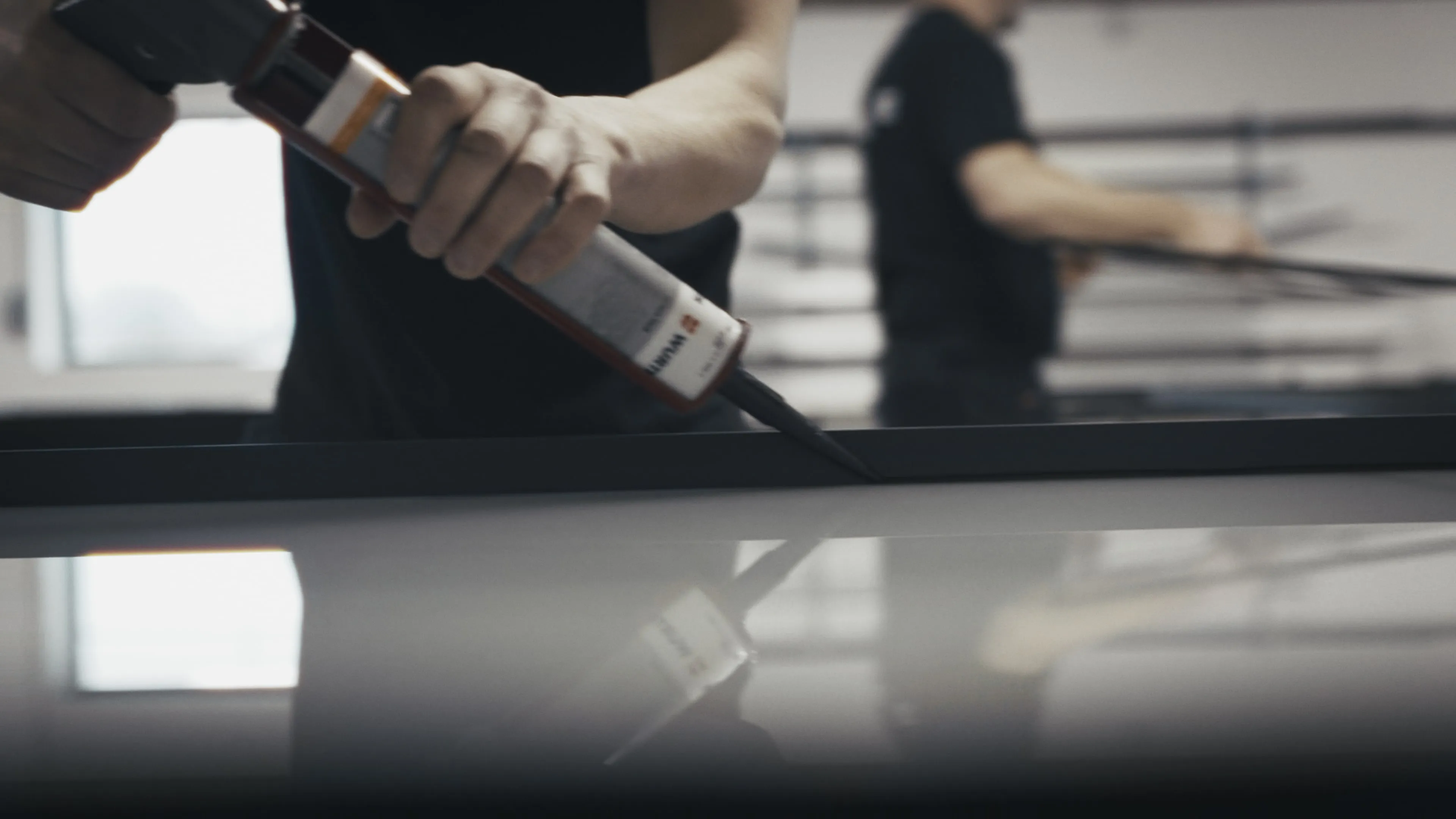 Person påfører tæt tætningsmiddel langs kanten af et bord eller panel med en fugepistol.