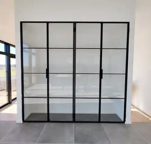 Sort metal og glas rumdeler med dobbelte døre i et lyst rum med gråt flisegulv.