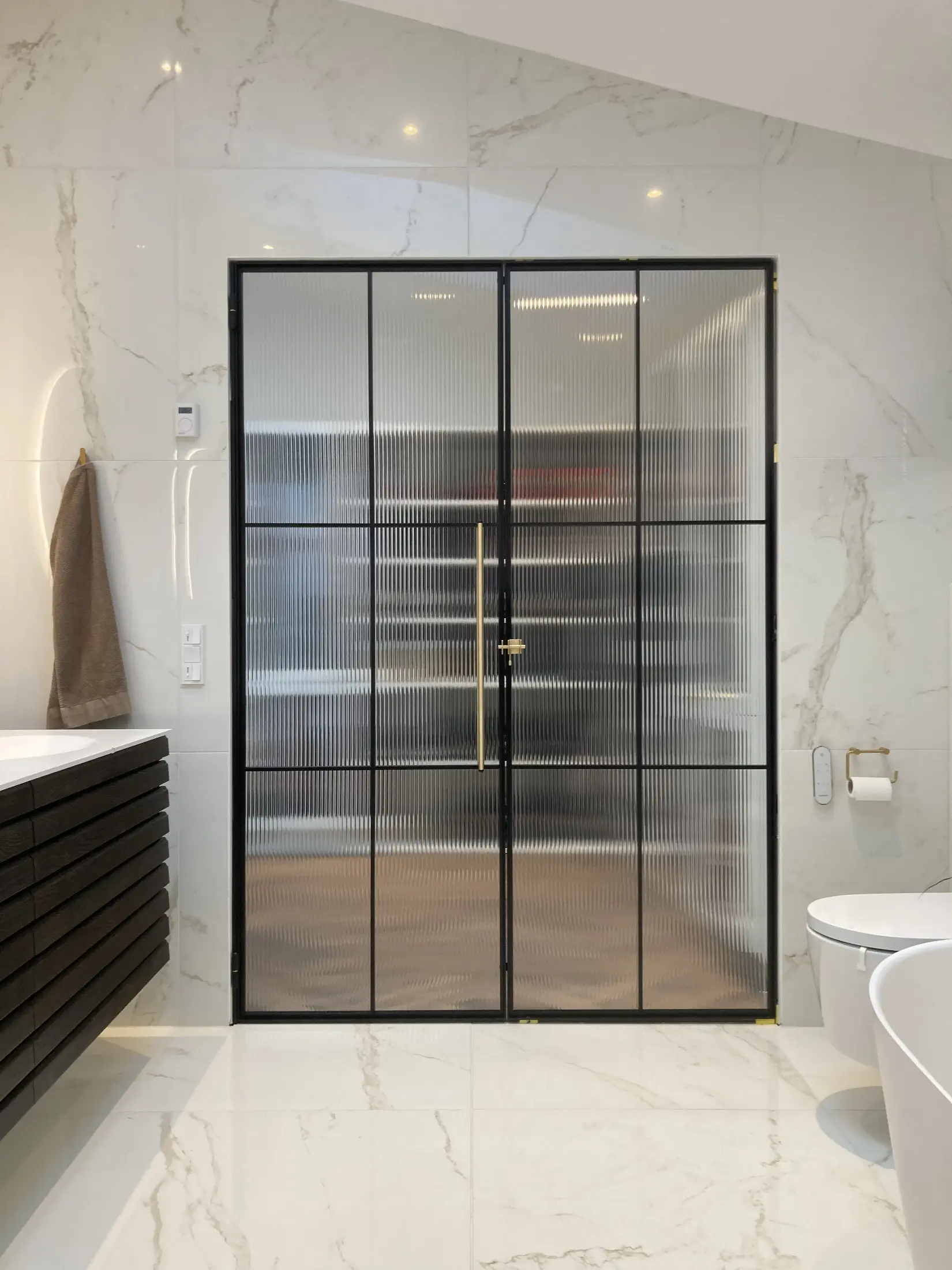 Moderne badeværelse med hvid marmorflisevæg, sort rammedør med ridsede glas, og toilet med gulvmonteret bidet.