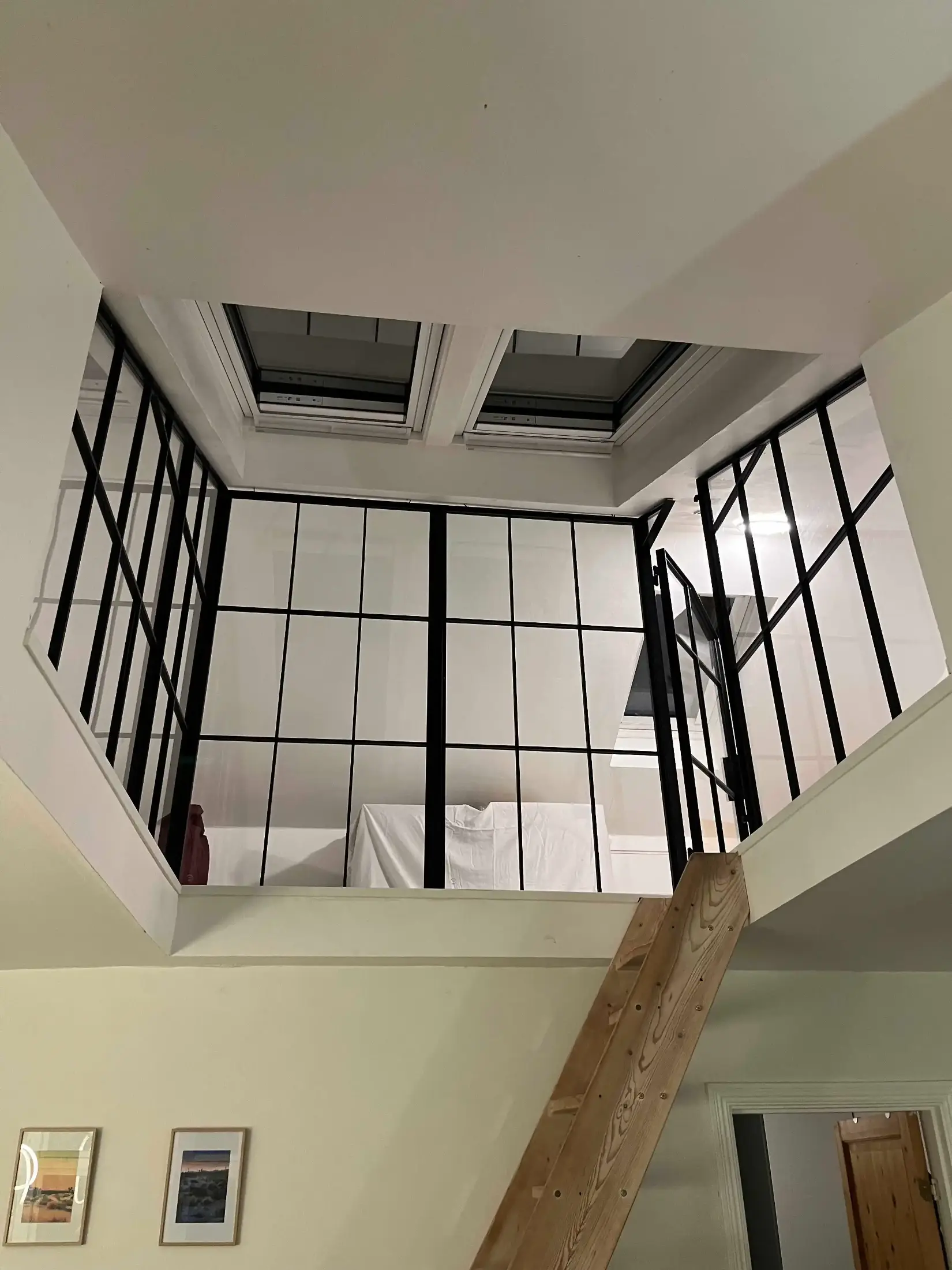 Indendørs trappe med trætrin, der fører op til en hems med sorte metal- og glasvægge og to ovenlysvinduer i loftet.