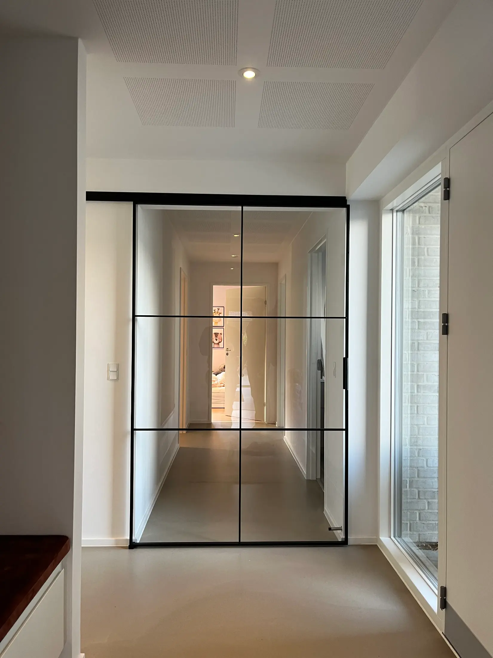 Gang med stor spejldør opdelt i ni firkanter, der reflekterer en anden dør og vægdekorationer.