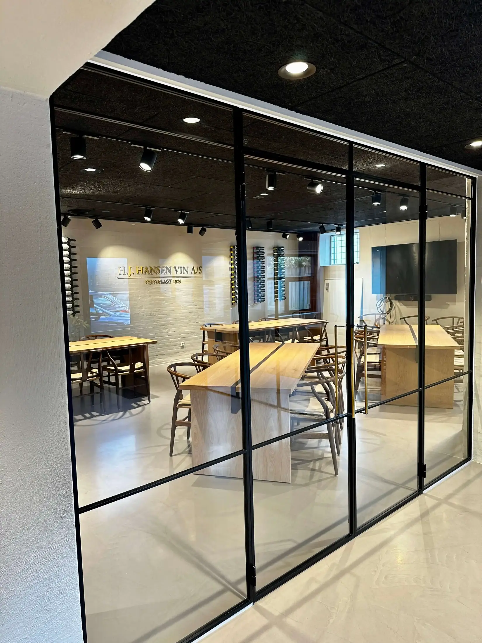 Mødelokale med glasvægge, træborde og mørke træstole, væggen har skilt med H.J. Hansen Vin A/S indgraveret.