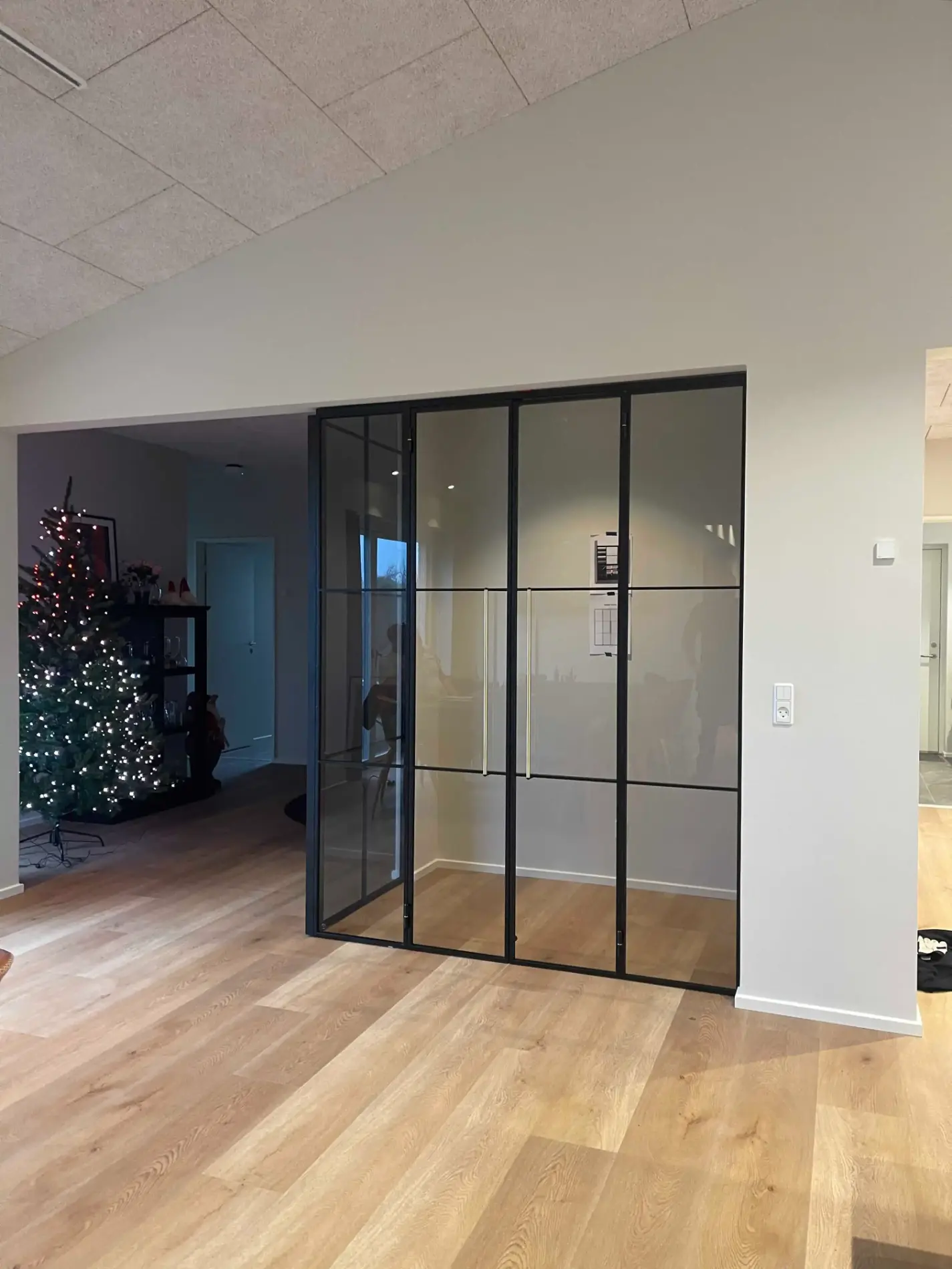 Moderne rum med trægulv og store glasdøre med sort metalramme, juletræ med lys i hjørnet.