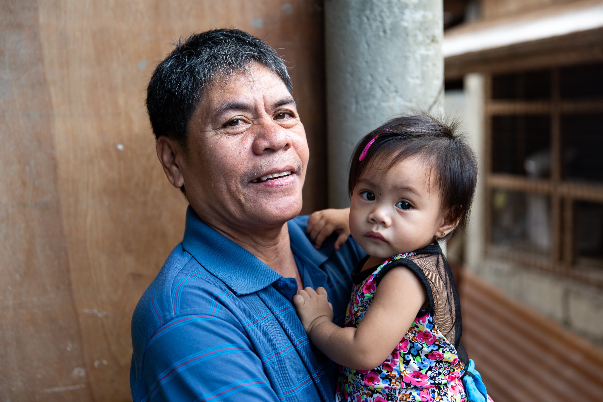 Older man in blue shirt holding a young girl wearing a colorful floral dress with a pink hair clip.