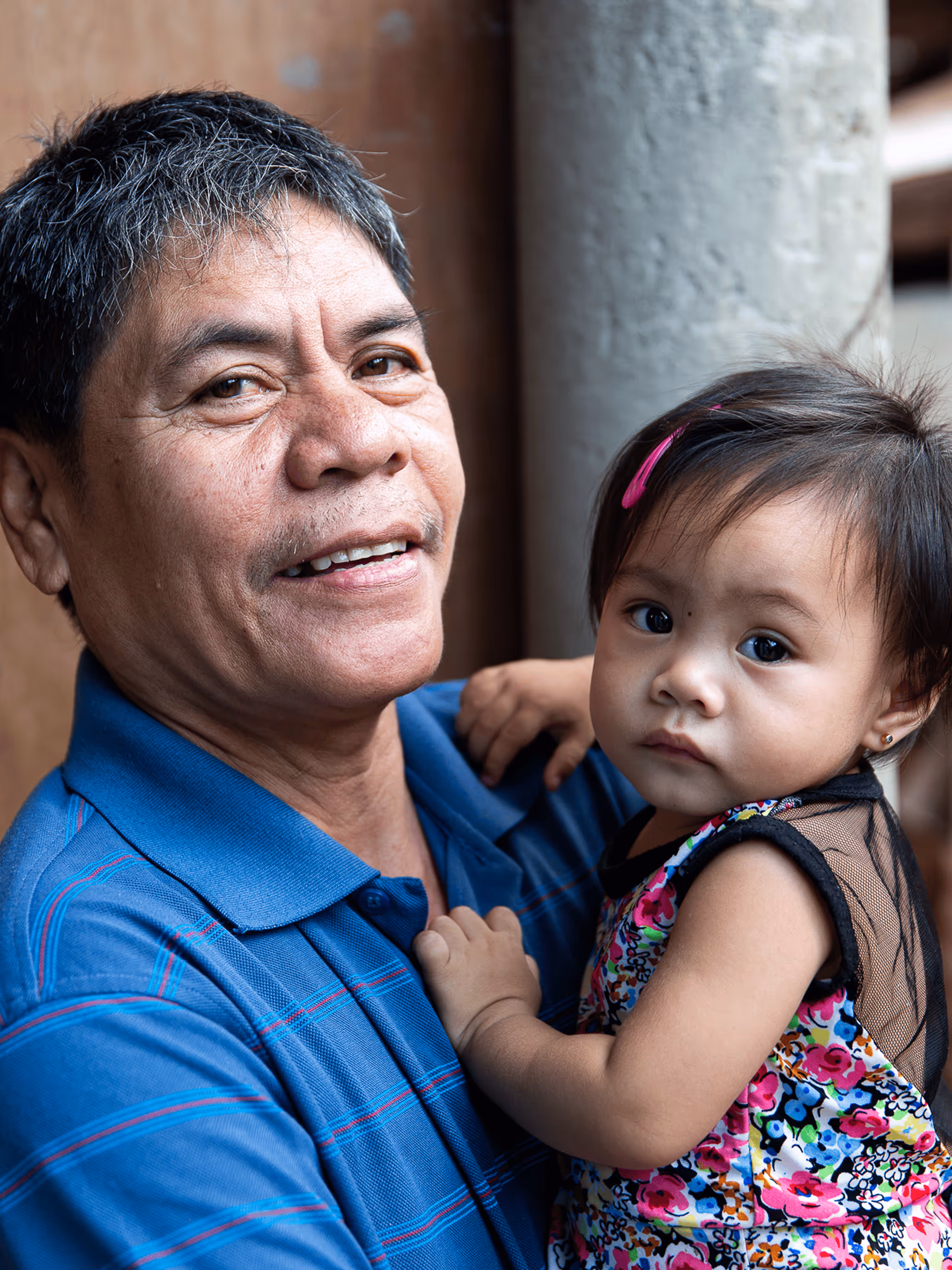 Homme tenant une petite fille portant une robe fleurie multicolore avec une pince rose dans les cheveux.