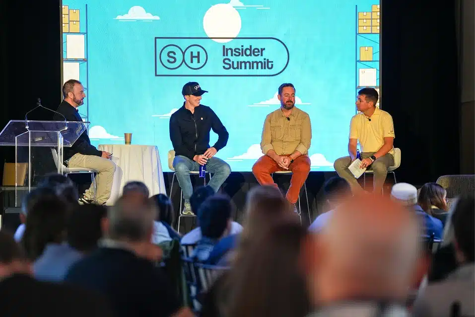 Four men seated on stage in a panel discussion at SH Insider Summit with an audience watching.