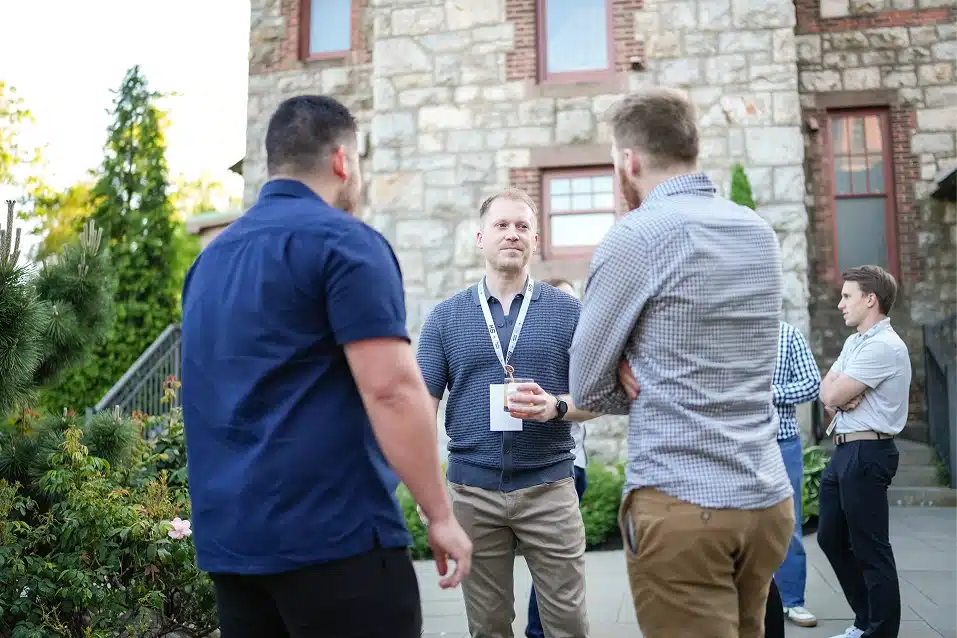 Group of men engaged in conversation outdoors in front of a stone building during daytime.