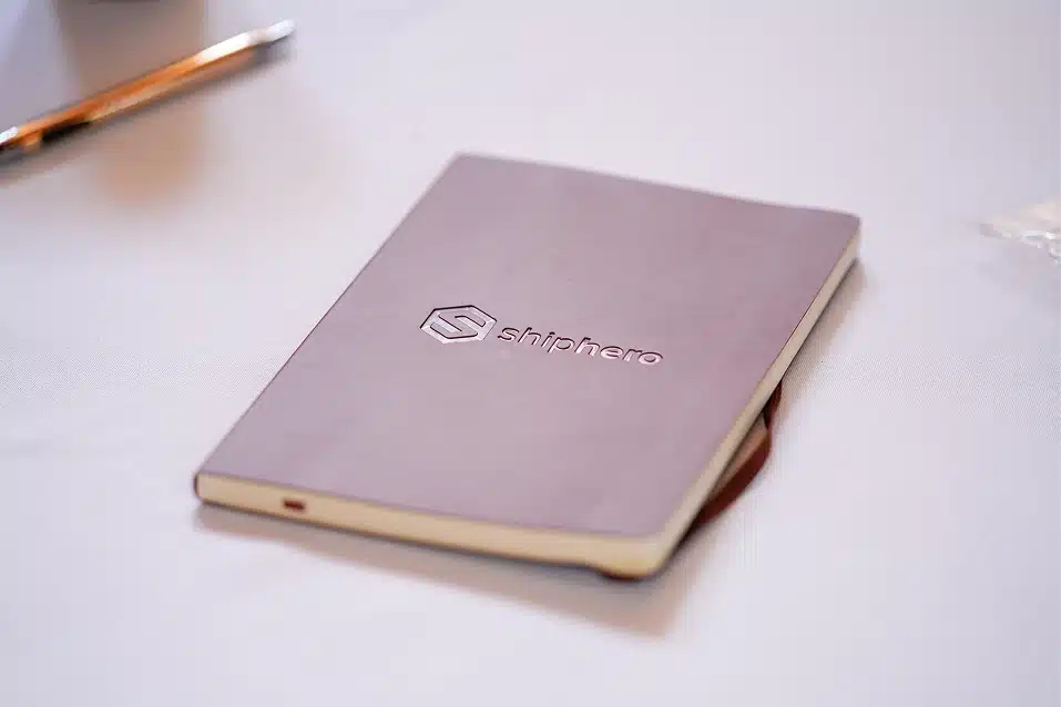 Closed notebook with a soft purple cover embossed with the Shiphero logo placed on a white surface.