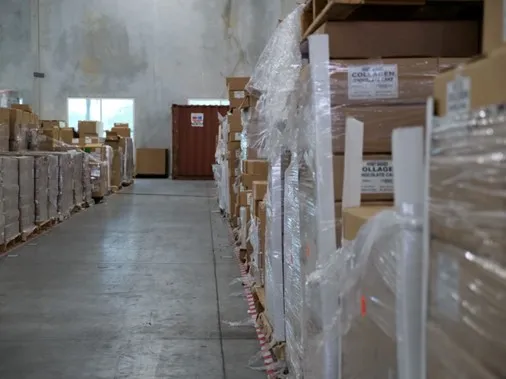 Warehouse aisle with shelves stocked with stacked cardboard boxes wrapped in plastic.