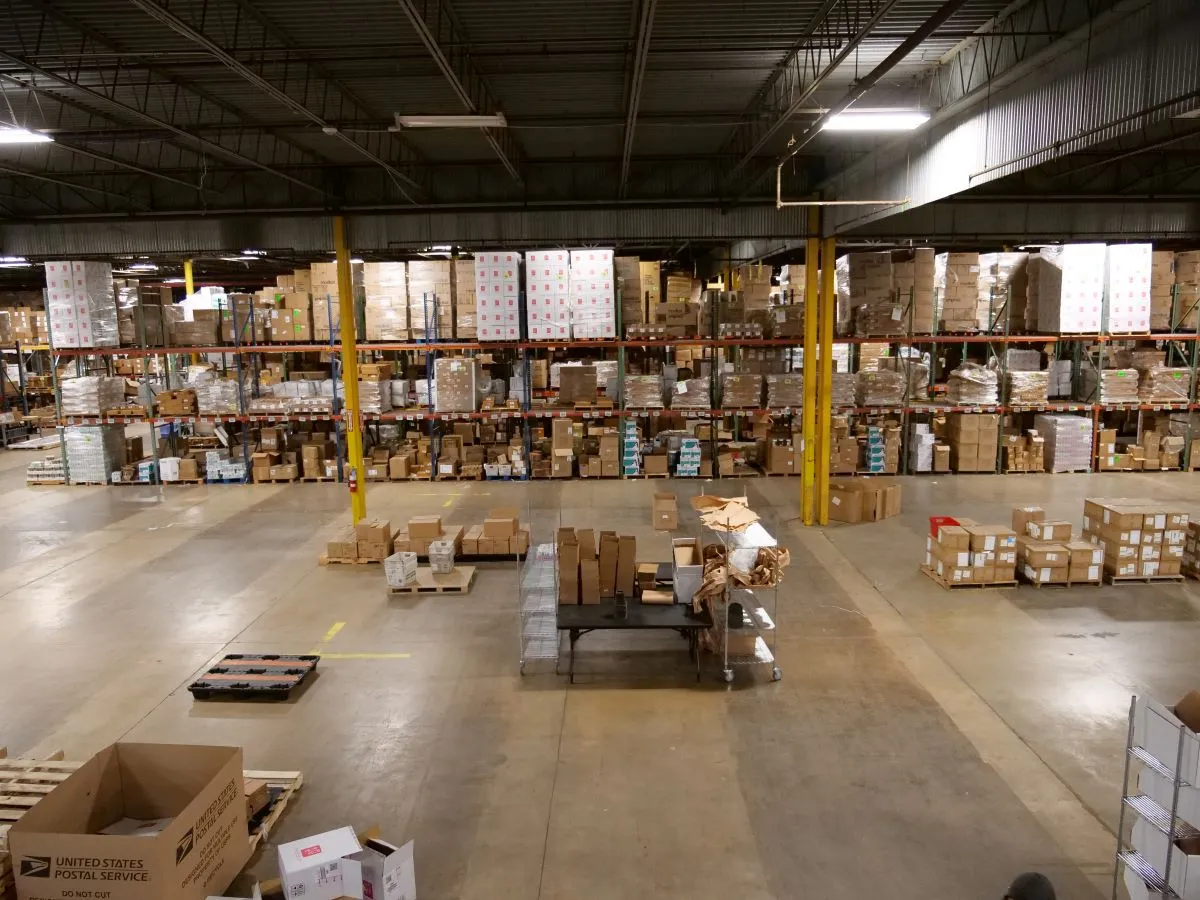 Warehouse interior with shelves stacked high with brown boxes and pallets on the concrete floor.