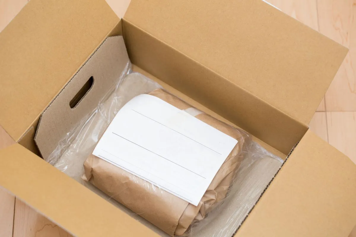 Open cardboard box with a brown paper-wrapped package inside, padded with air cushion wrap.