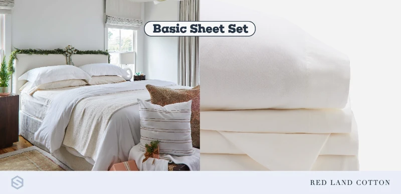 Stack of cream basic sheet set beside a neatly made bed in a cozy bedroom with pillows.