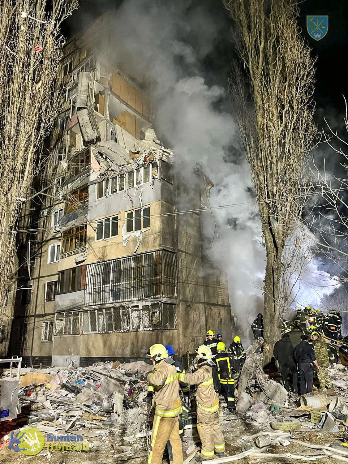 Eingestürztes Wohngebäude bei Nacht mit Rauch, Feuerwehrleute und Rettungskräfte beim Einsatz im Trümmerfeld.