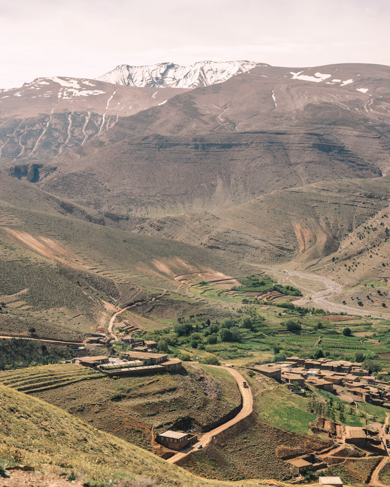 Village Zawiyat Oulmzi avec des maisons en terre au pied de montagnes arides avec des sommets de haut atlas marocain enneigés en arrière-plan
