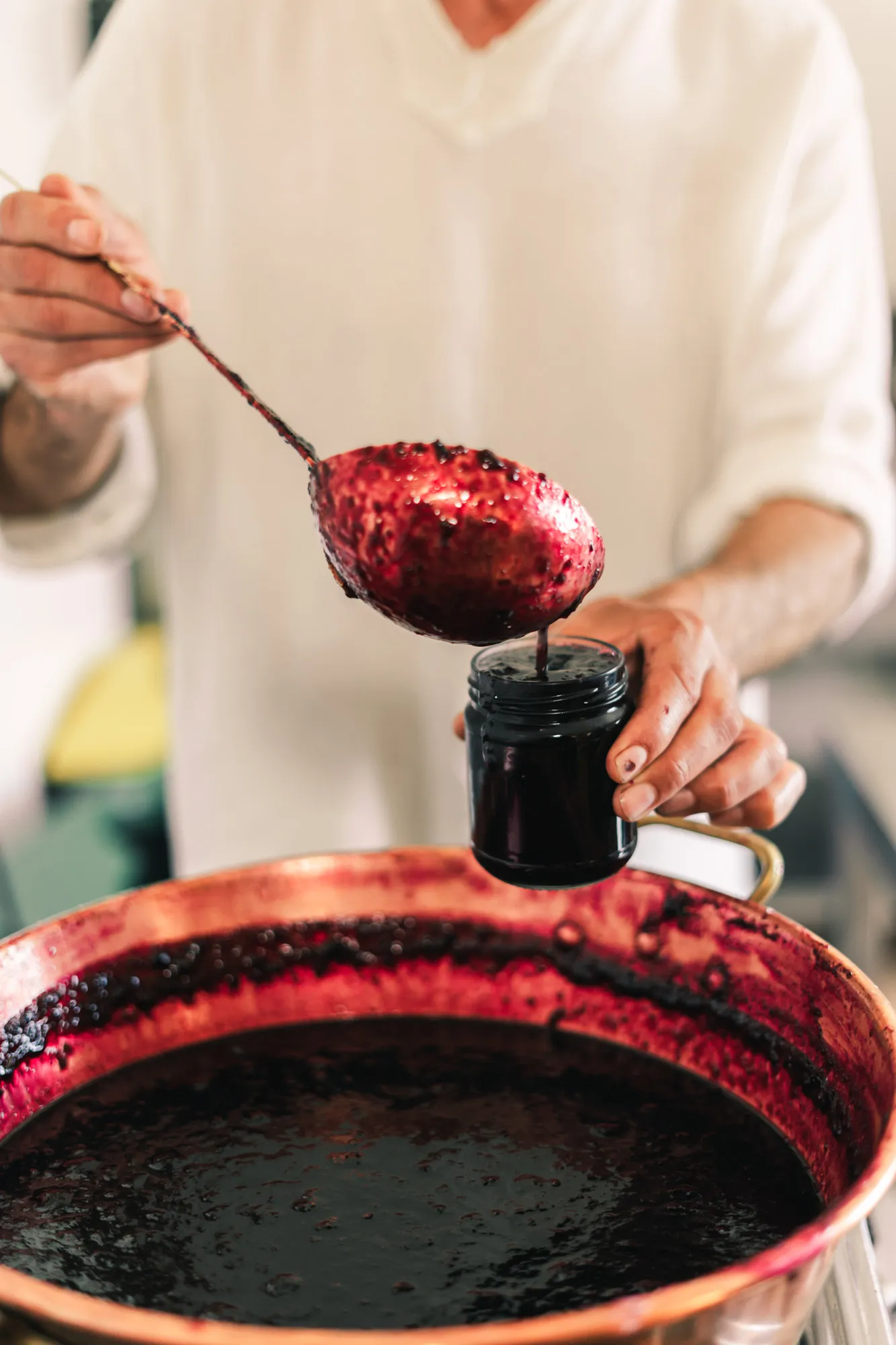 Saïd de Touda ecolodge versant de la confiture bio de terre de l'atlas de baies foncées d'une grande casserole dans un petit pot en verre.