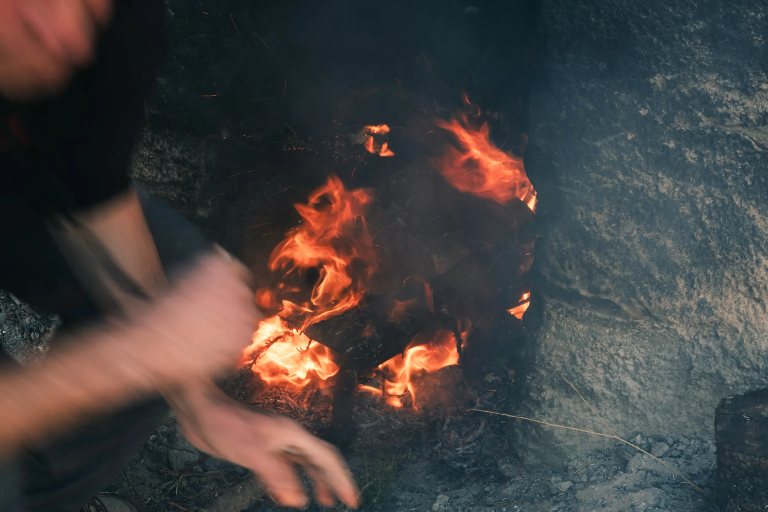 Mains floues ajustant des bûches dans un feu du hammam traditionnel marocain de touda ecolodge allumé dans une structure en pierre.
