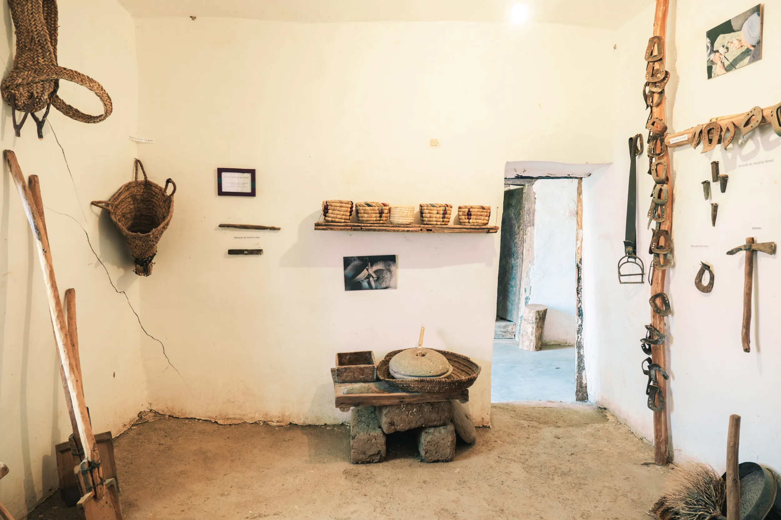 Intérieur de l'ecomusée amazigh traditionnelle avec outils agricoles de le vallée bougemez accrochés aux murs, paniers en osier et meule en pierre sur un support en pierre.