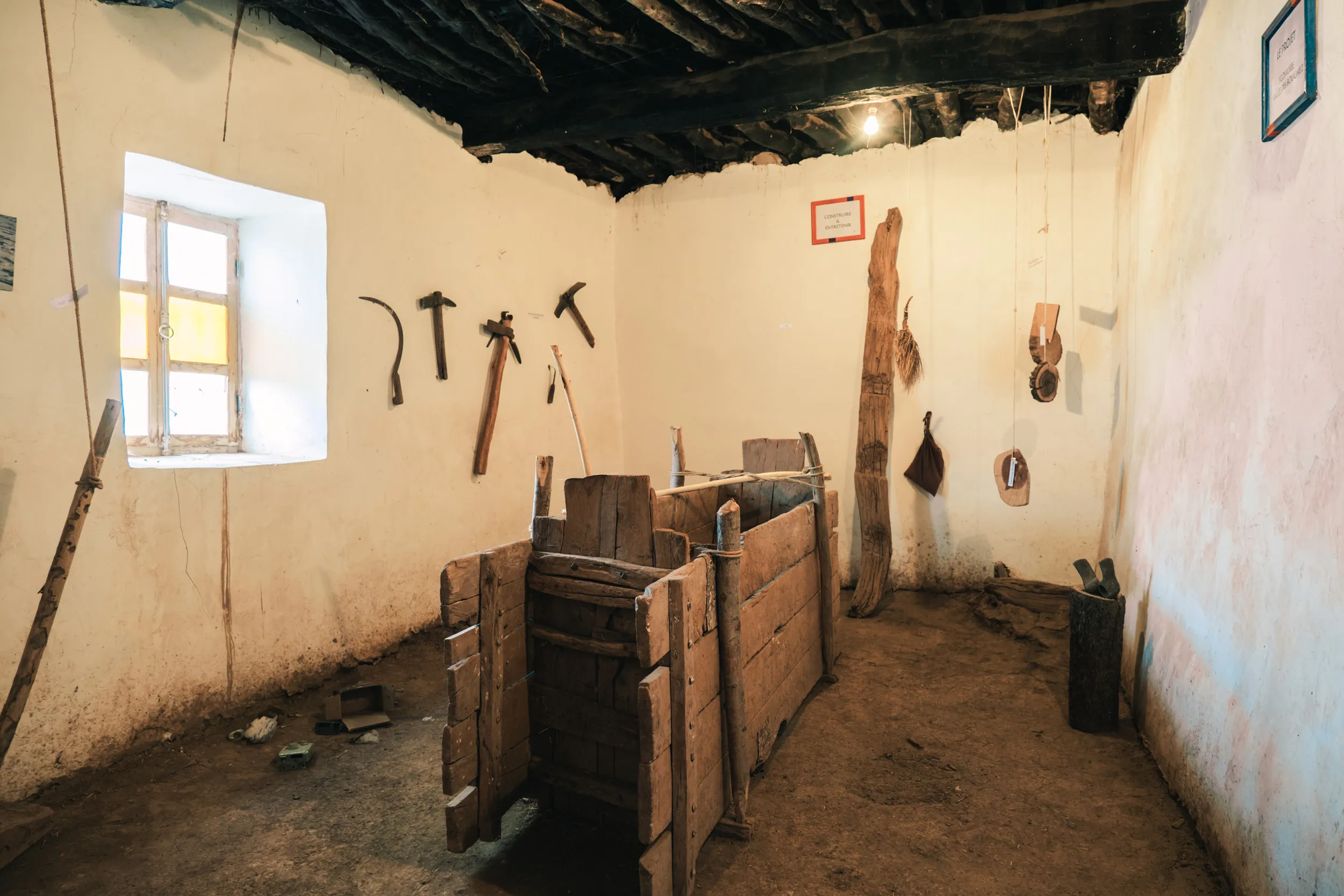 Intérieur de l’écomusée de la Vallée Heureuse à visiter, avec des outils agricoles traditionnels marocains en bois accrochés aux murs et une structure en bois au centre de la pièce, dans la vallée des Aït Bougmez, Haut Atlas marocain.