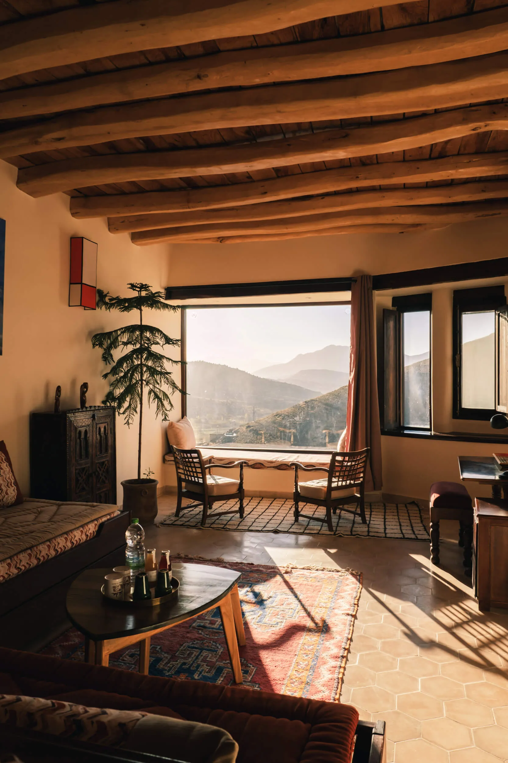Salon à Touda ecolodge auberge au Maroc avec poutres en bois, deux fauteuils devant une grande fenêtre offrant une vue sur les montagnes de la vallée ait bougmez au maroc.