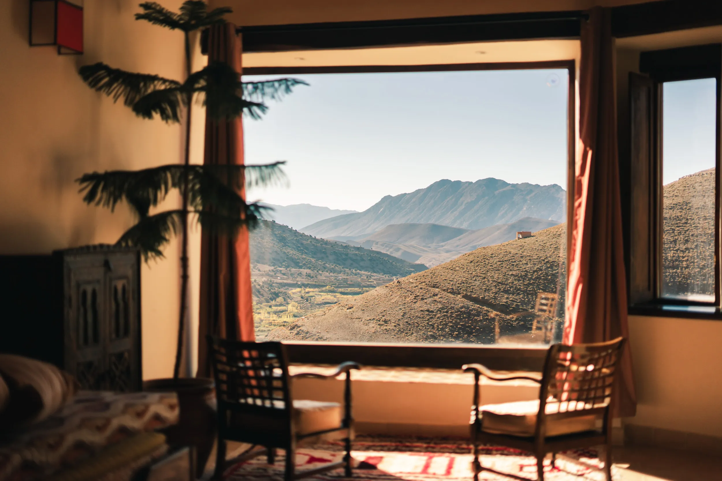 La suite de Touda ecolodge avec deux fauteuils devant une grande fenêtre offrant une vue dégagée sur des collines et des montagnes de la vallée ait bougemez