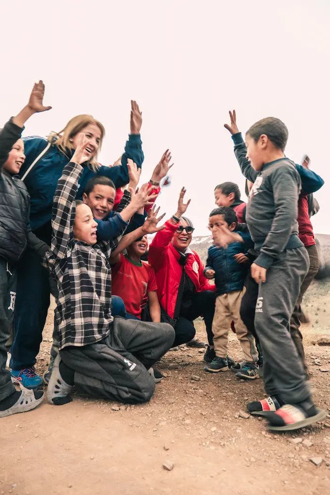 Un moment de joie partagée entre des bénévoles et un groupe d'enfants du village dans le Haut Atlas, illustrant l'engagement social et les échanges humains au cœur des projets solidaires de l'écolodge et l’association arbre du voyageur.