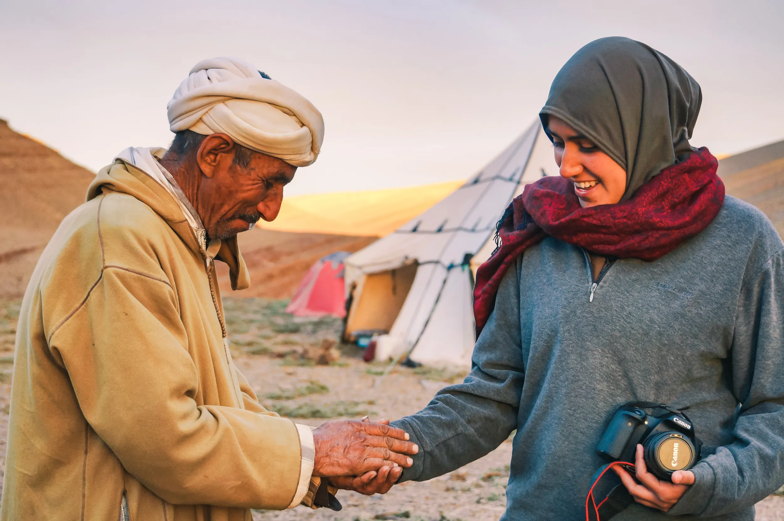 Un nomade amazigh marocain et une femme se serrent la main devant une tente nomade au haut atlas marocain, la femme tenant un appareil photo.