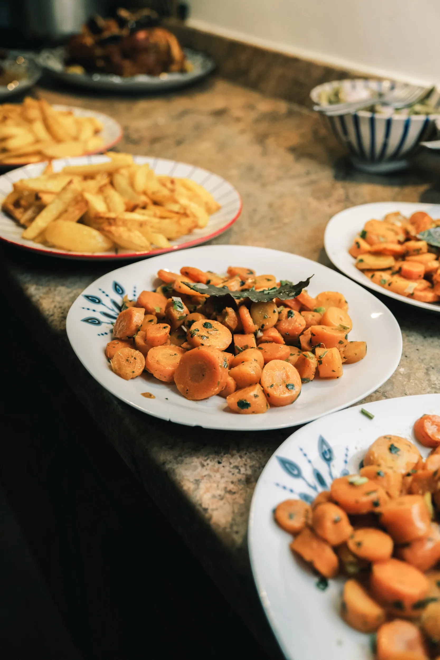 Assiettes sur un comptoir dans la cuisine de touda ecolodge contenant des carottes sautées avec des herbes et des frites.
