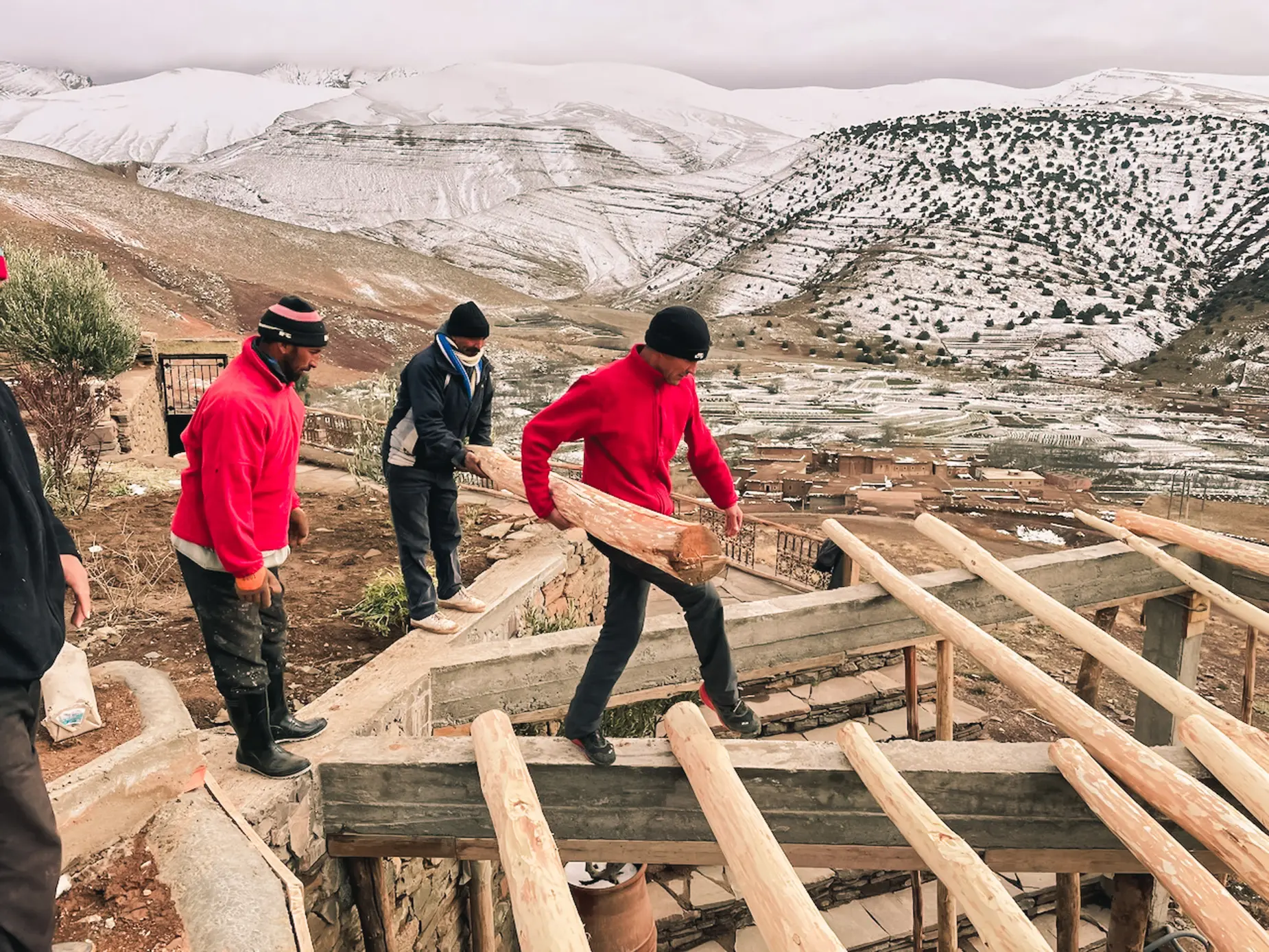 Des ouvriers transportent une poutre en bois sur Touda ecolodge entrain d'être construite face aux montagnes enneigées au vallée heureuse Ait Bougemez.