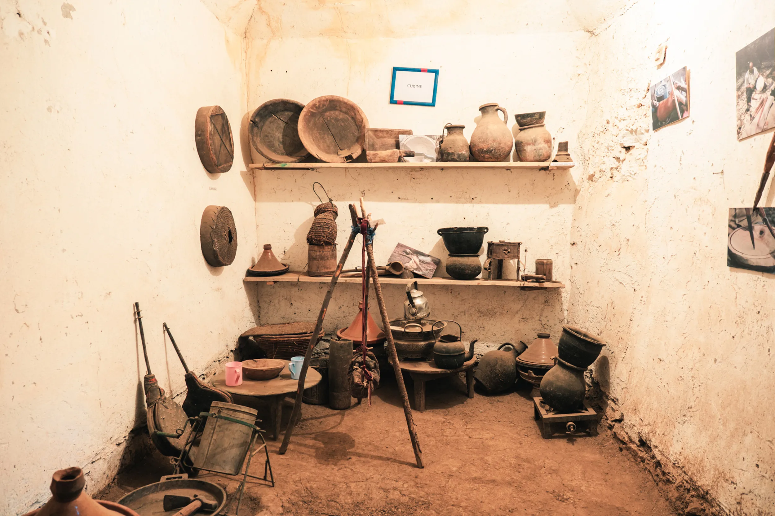 Intérieur de l'ecomusée de la vallée bougemez avec des poteries anciennes, des ustensiles en terre cuite et des objets en bois sur des étagères et le sol en terre battue.