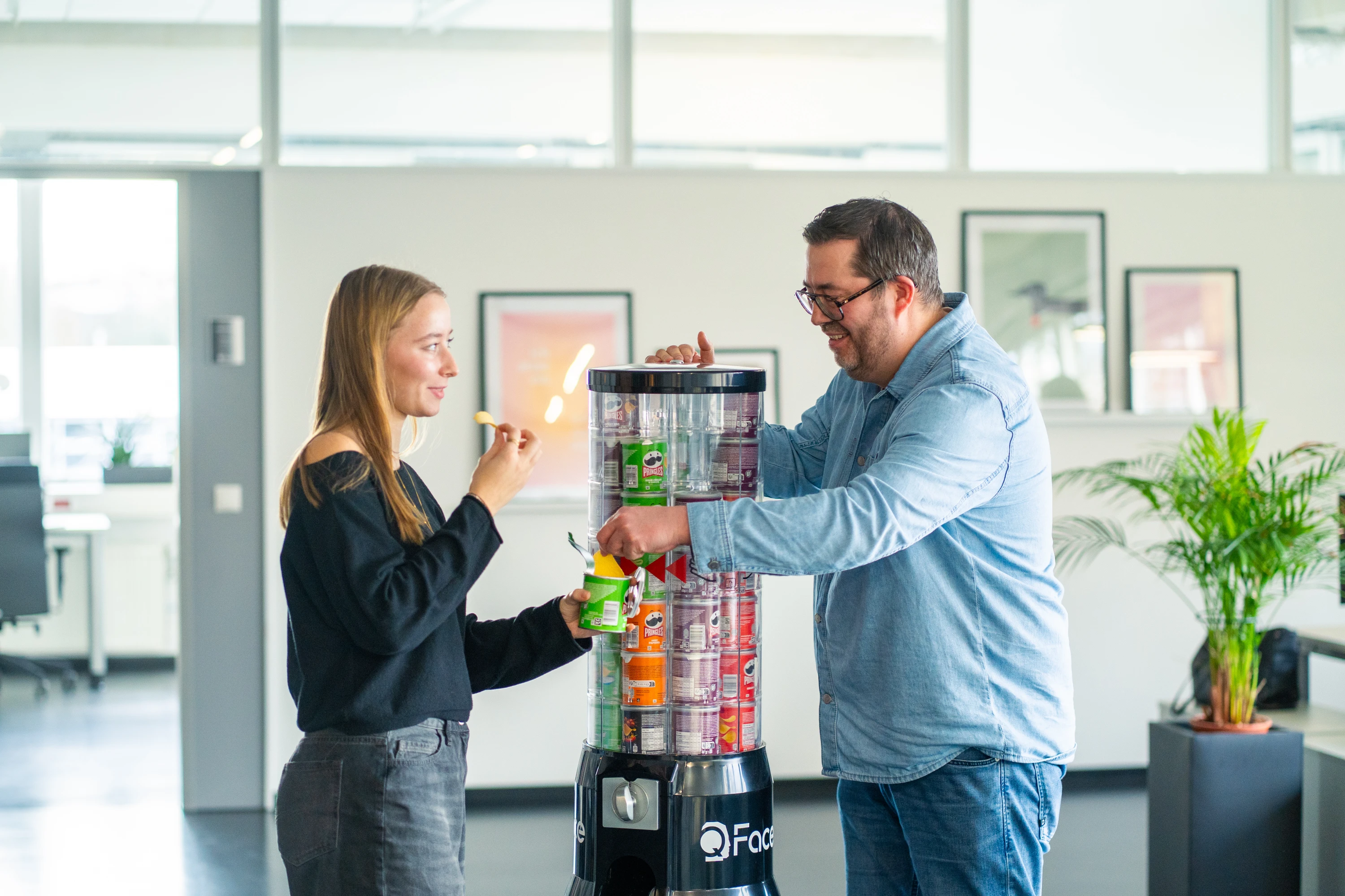 Frau und Mann nehmen Pringles-Chips aus einem schwarzen, zylindrischen Spender in einem modernen Büro.