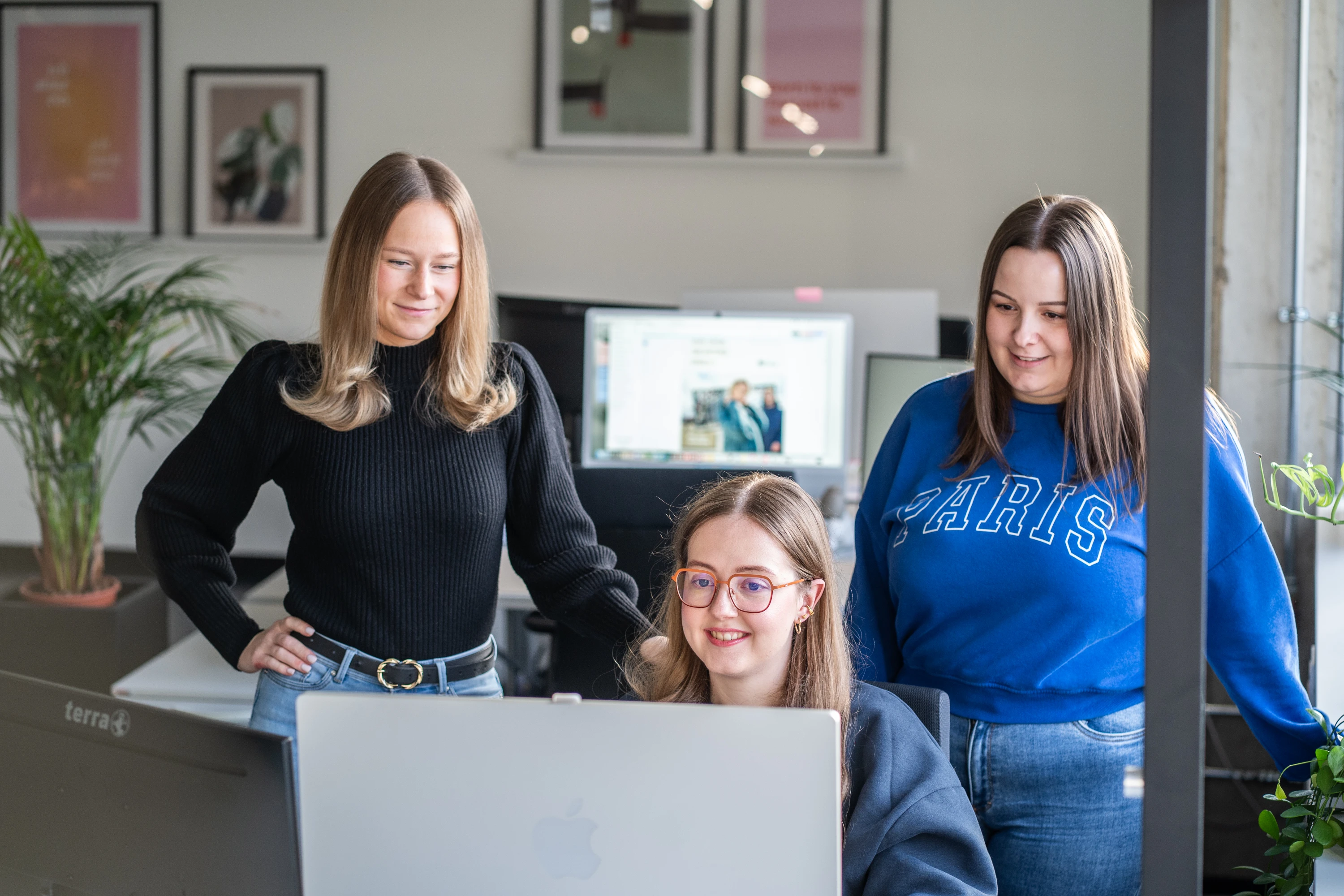 Drei junge Frauen arbeiten gemeinsam an einem Computer in einem modernen Büro.