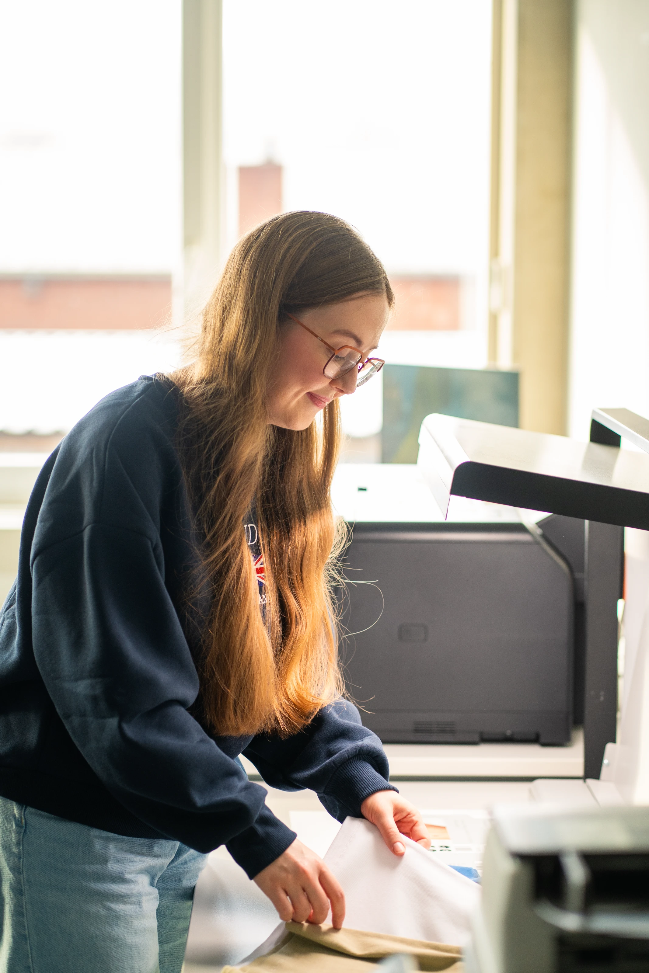 Junge Frau mit langem Haar und Brille, die an einem Scanner oder Drucker arbeitet.