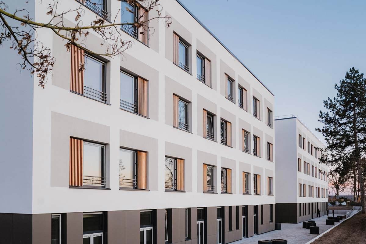 Moderner, mehrstöckiger Gebäudekomplex mit weißen Wänden, rechteckigen Fenstern und Holzläden, umgeben von Bäumen. Neubau des Anbaus der Stadtklinik Frankenthal Pfalz