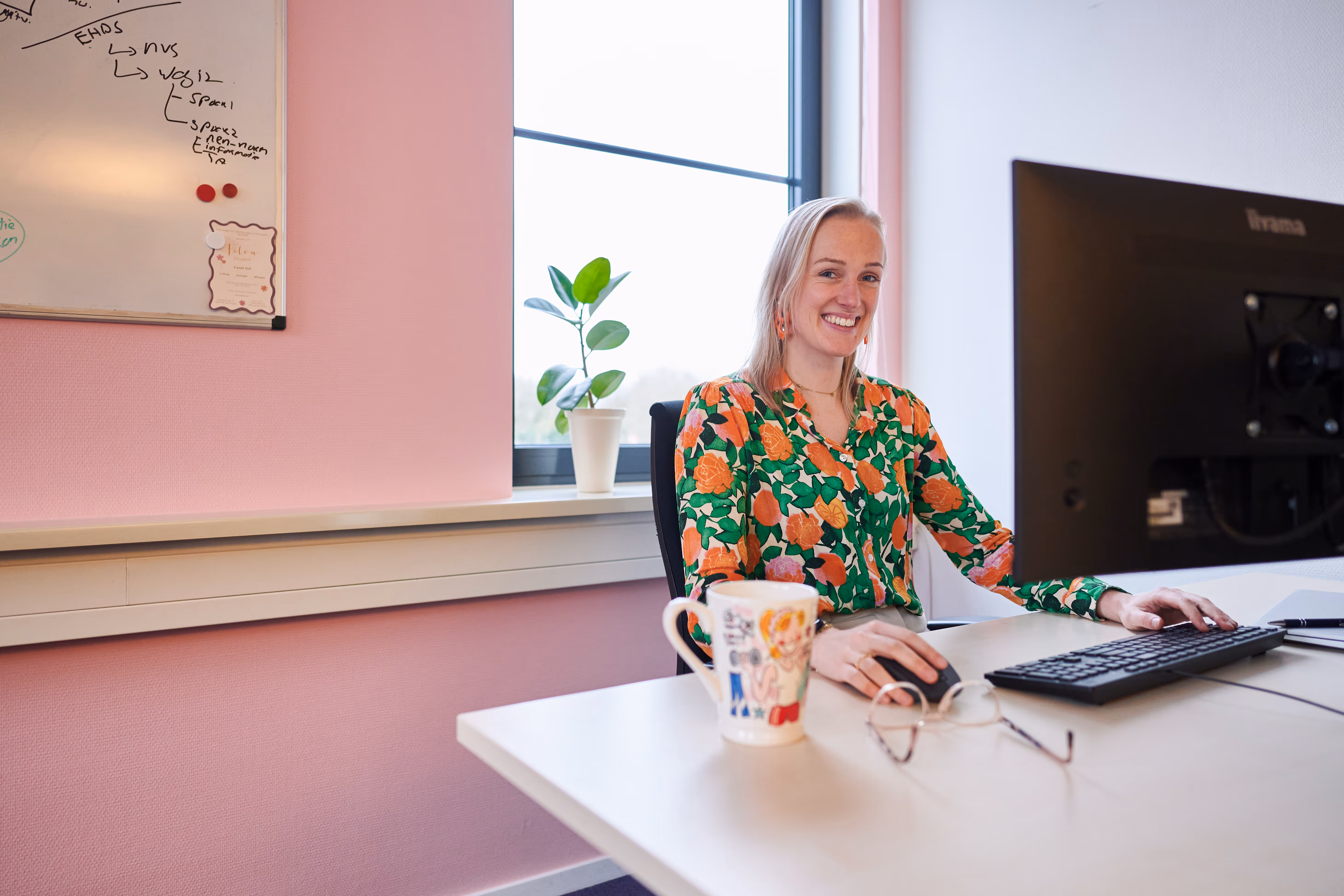 Jonge meid met kleurige blouse glimlacht naar camera vanachter de computer