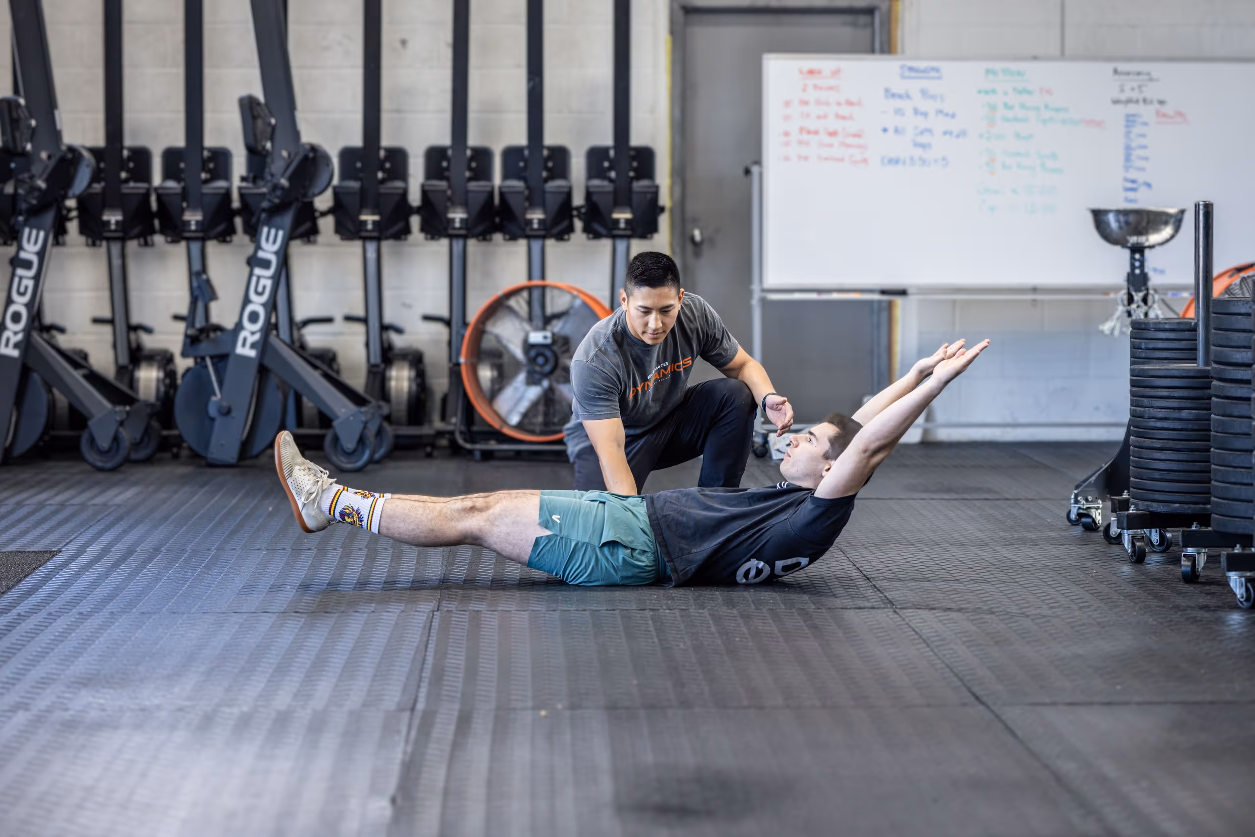 Fitness trainer coaching a man lying on the floor with legs and arms extended during a workout in a gym. massapequa physical therapy