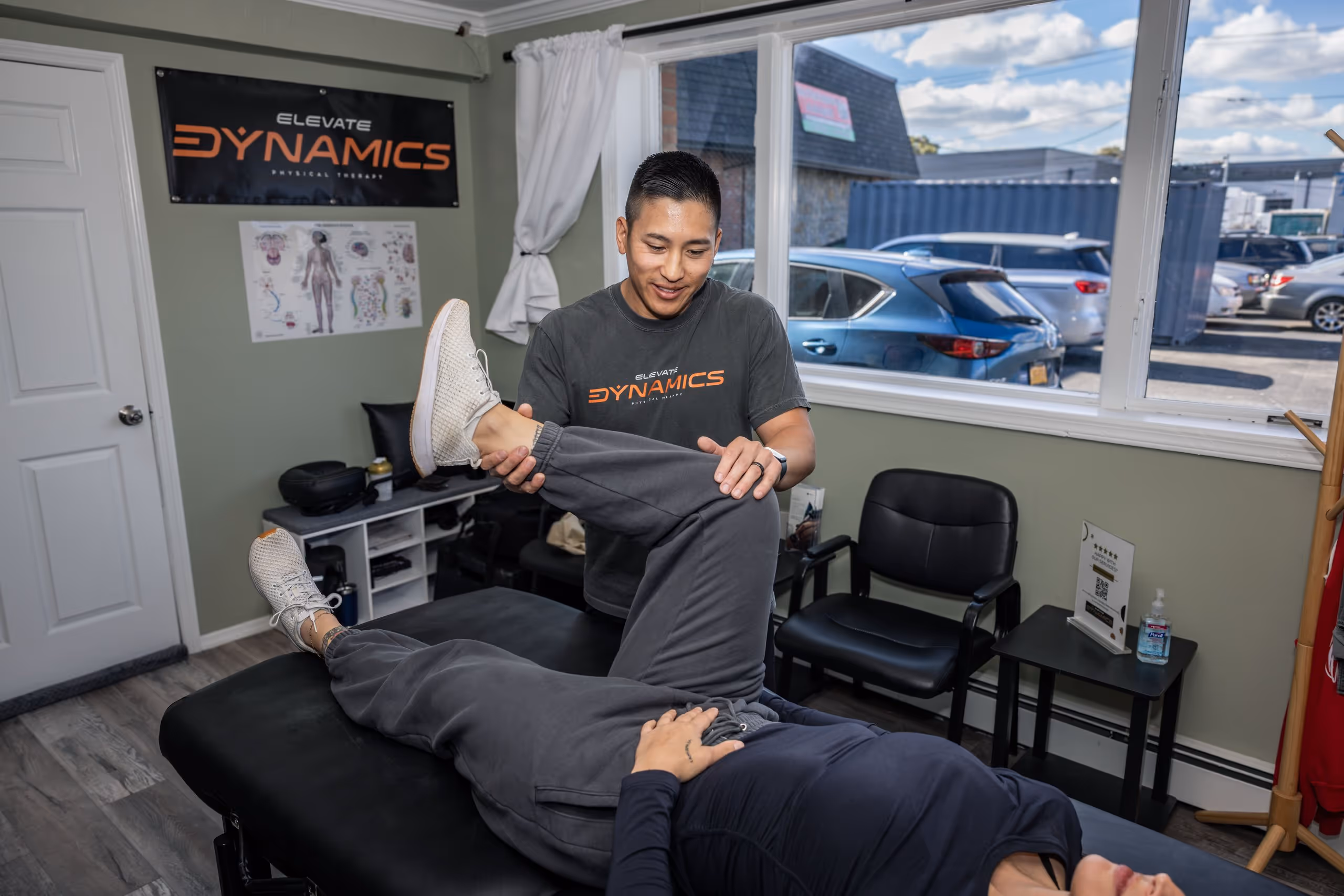 Elevate Physical therapist in an Elevate Dynamics shirt stretches a patient's leg on a treatment table in a therapy room. physical therapy massapequa ny